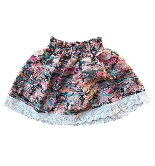 A high-waisted, tiered ruffle skirt featuring a dense multicolor collage print and a white eyelet lace hem, displayed flat against a white background.